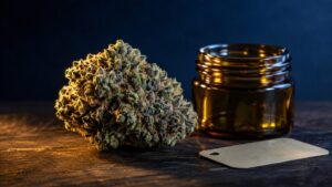Fleur de cannabis dense et résineuse à côté d'un bocal en verre ambré, sur un plan de travail en bois sombre